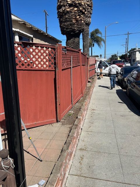 A man walking down a sidewalk next to a red fence