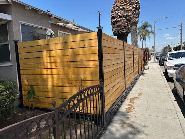 A wooden fence is along the sidewalk in front of a house.