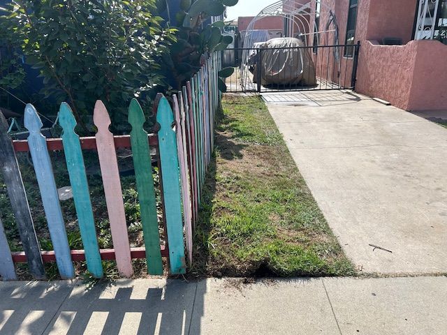 A man walking down a sidewalk next to a red fence