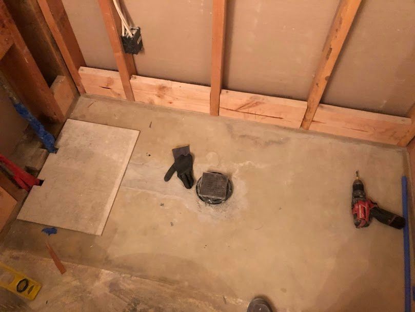 A drill is sitting on the floor of a bathroom under construction.