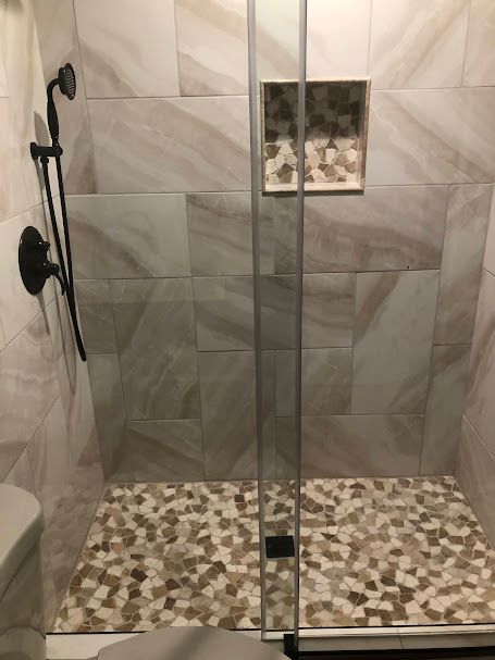 A walk in shower with a tiled floor and a glass door.