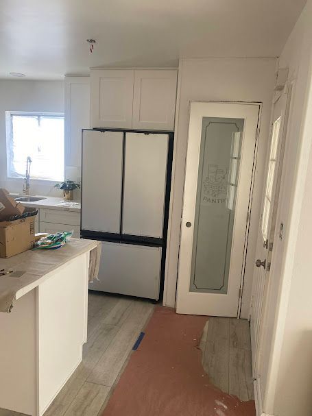 A kitchen with white cabinets , a refrigerator and a glass door.