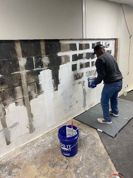 A man is painting a wall next to a blue bucket.