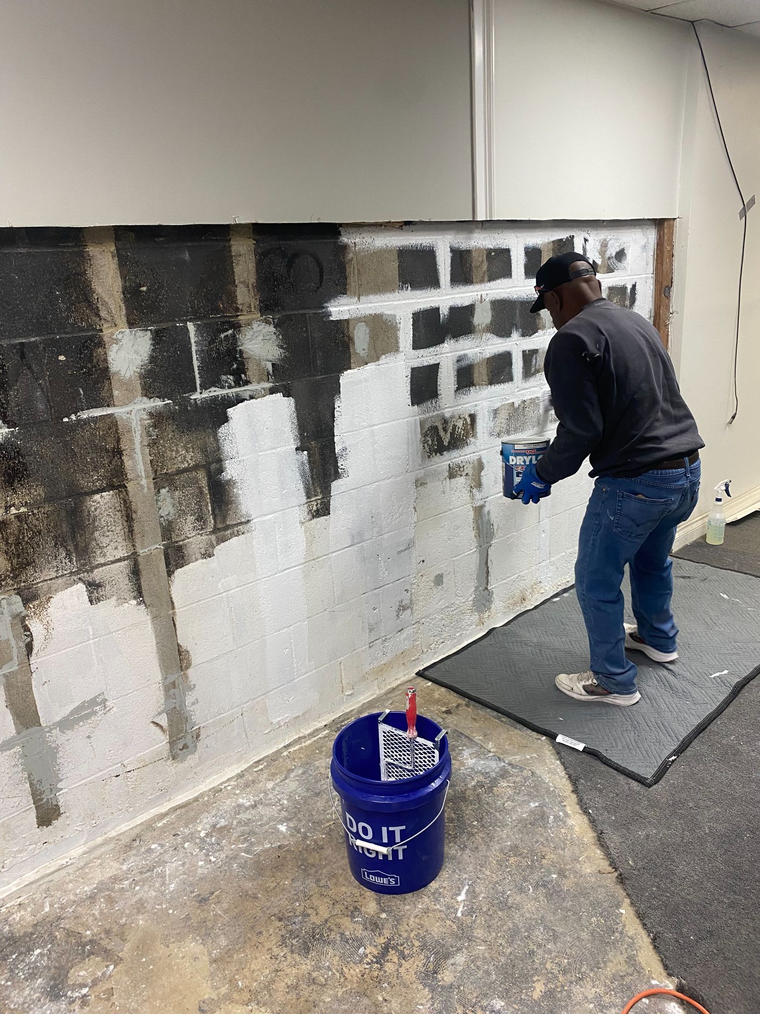 A man is painting a wall next to a blue bucket.