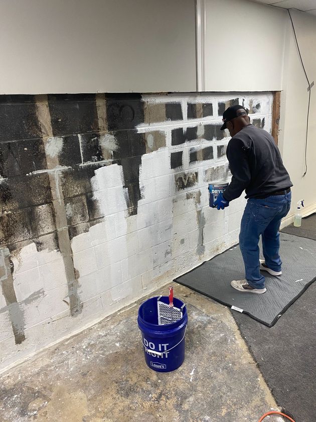 A man is painting a wall next to a blue bucket.