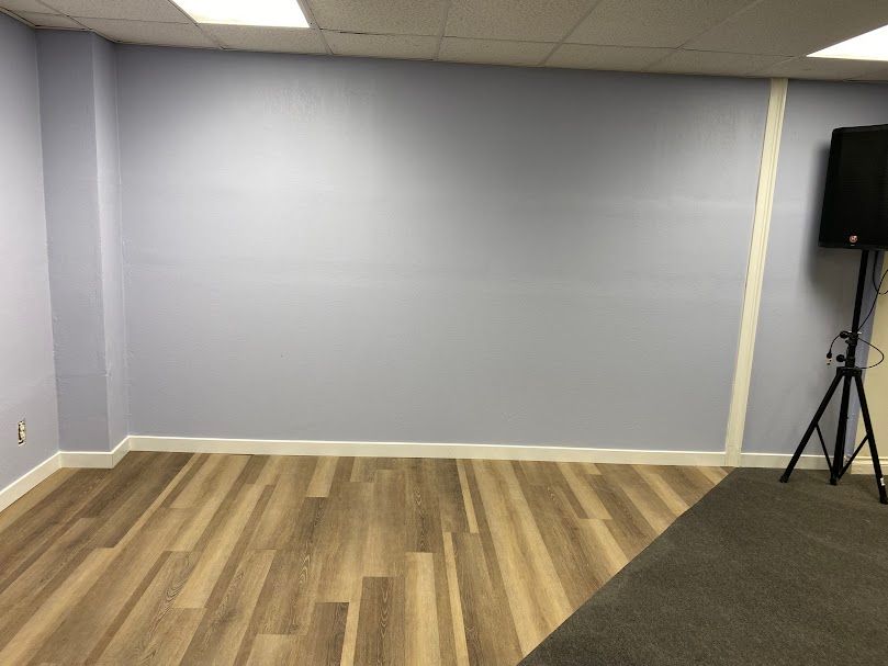 An empty room with a wooden floor and a speaker on a tripod.