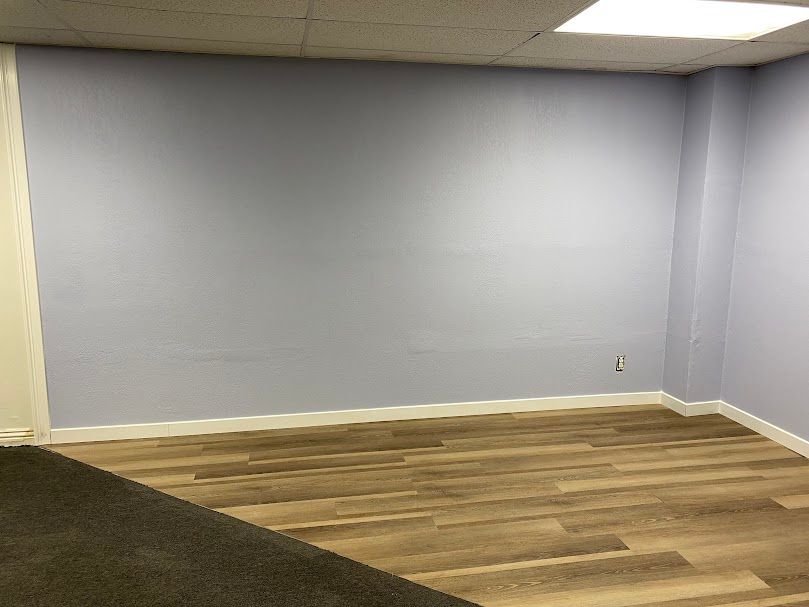 An empty room with a wooden floor and a gray wall.