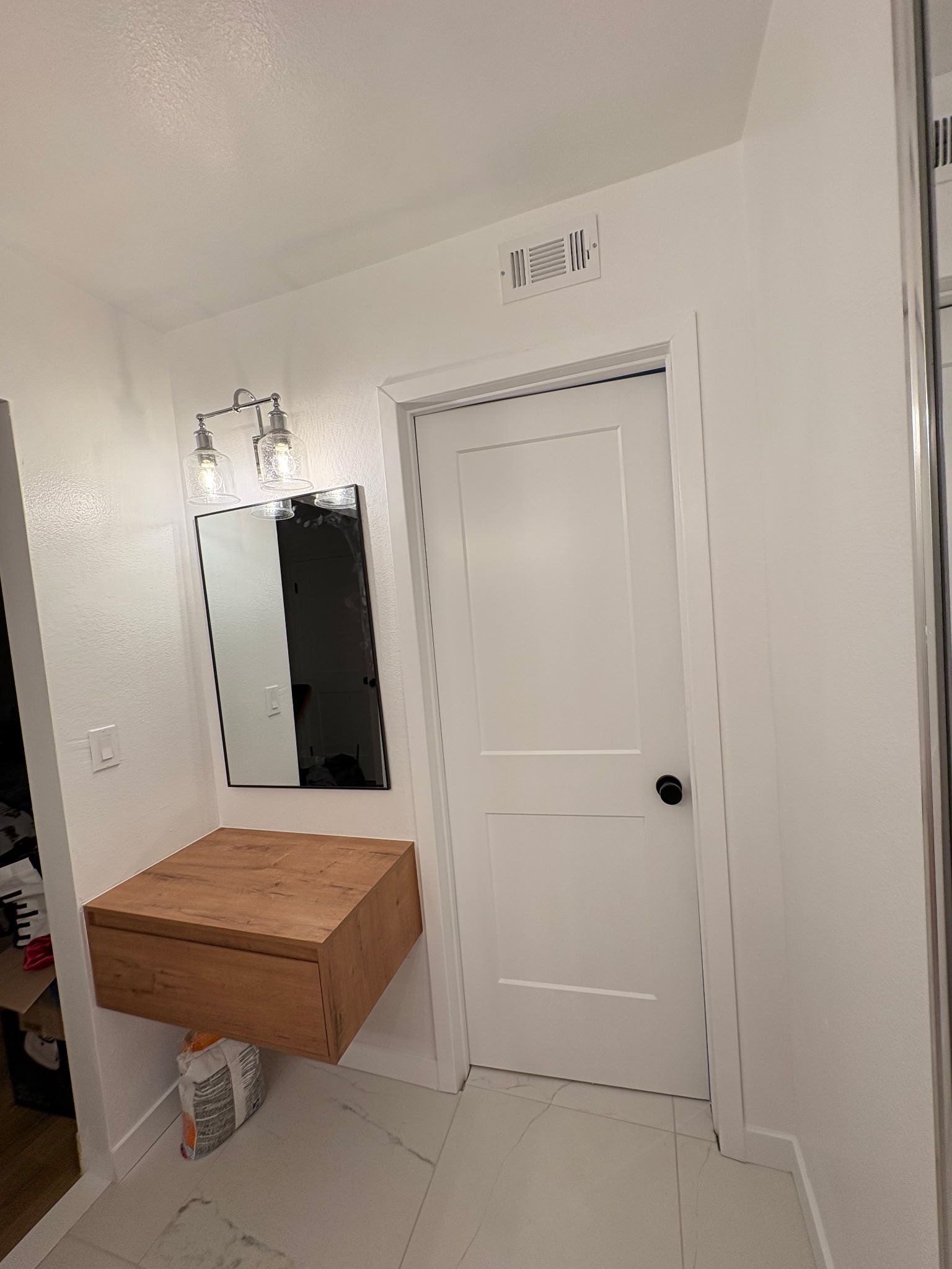 Bathroom with white walls, wood vanity, mirror, and white door.