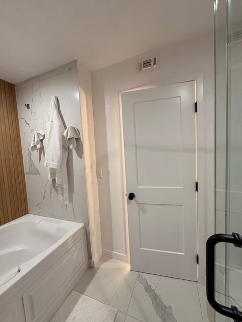 Bathroom with white door, tub, and marble tile. White towels hang.