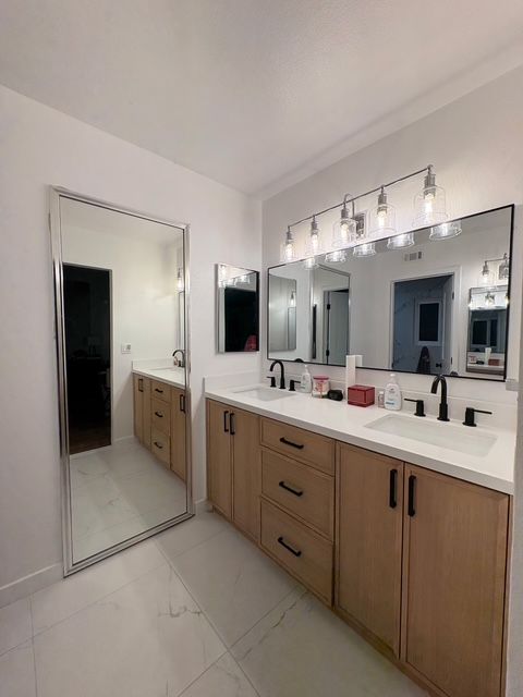 Modern bathroom with wood vanity, black fixtures, and three mirrors reflecting the space.