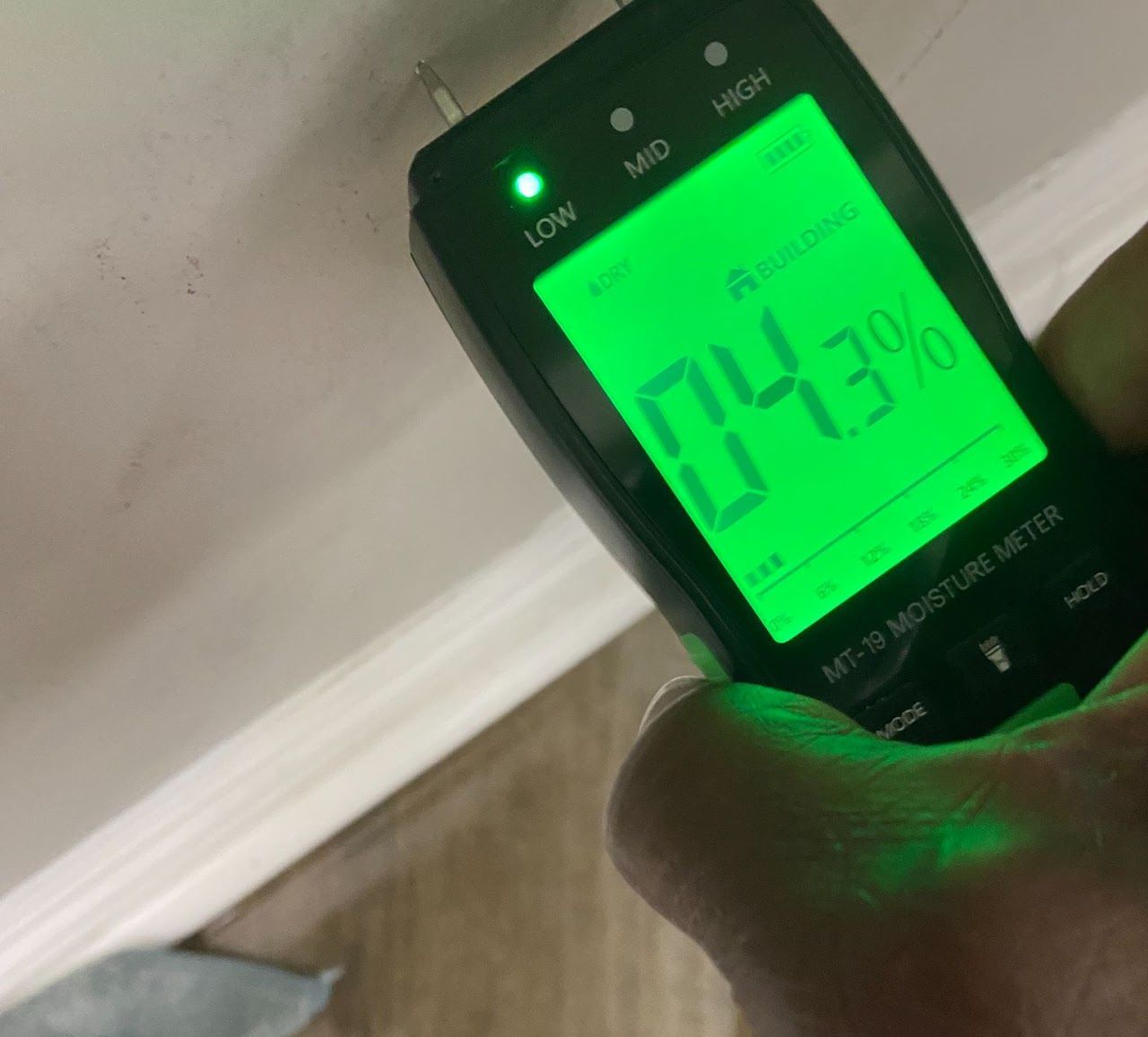 A person is holding a moisture meter with a green screen