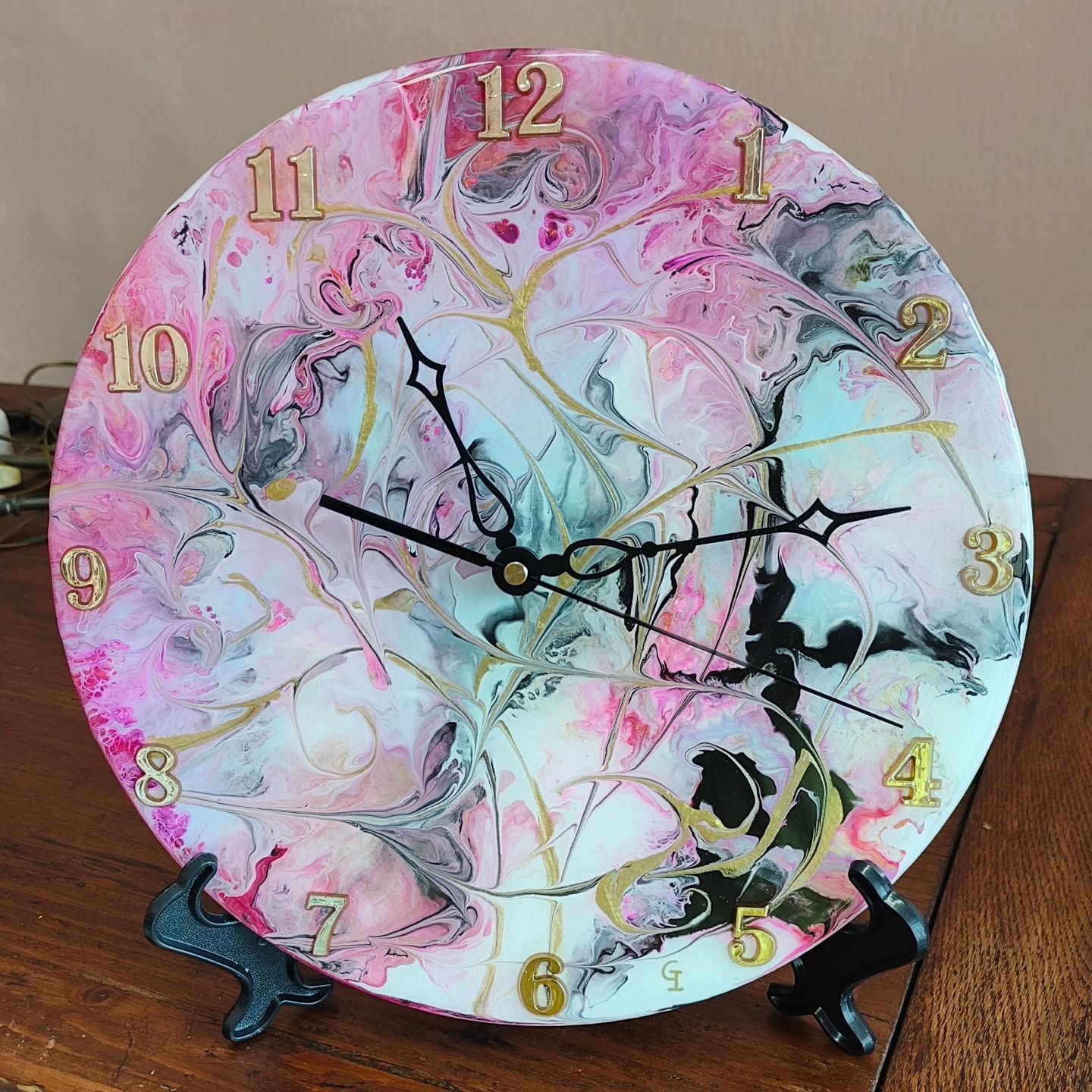 Un orologio rosa e bianco con numeri dorati è appoggiato su un tavolo di legno