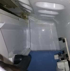 Interior of a refrigerator with white shelves and a blue lower compartment; partially open door.