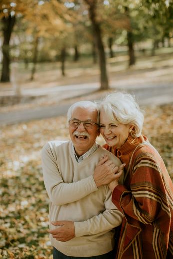 An elderly couple is hugging each other in a park.