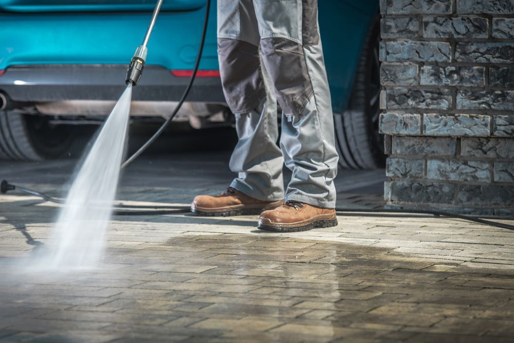 A Man is Using a High Pressure Washer to Clean a Driveway — DJ's Pressure Cleaning In Innisfail, QLD