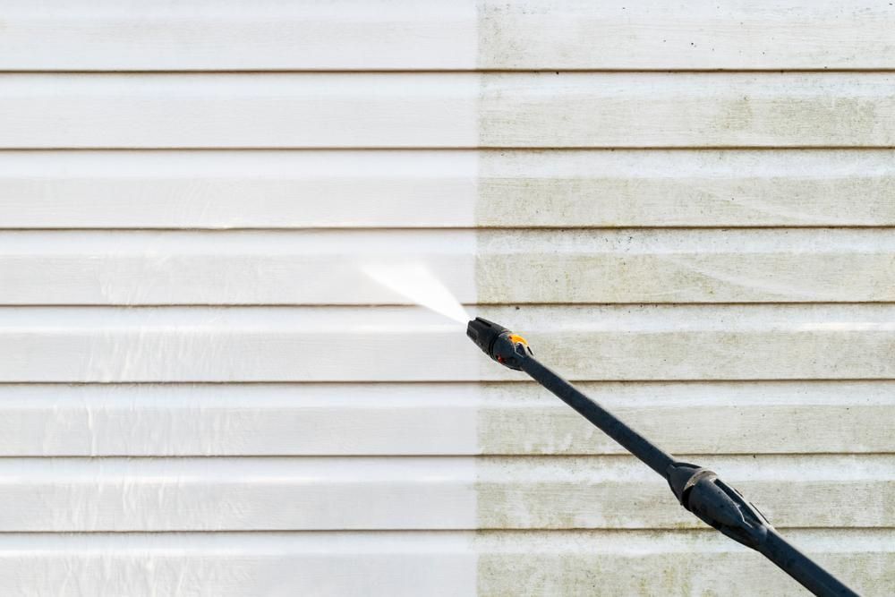 A Person is Cleaning the Side of a House With a High Pressure Washer — DJ's Pressure Cleaning In Carruchan, QLD