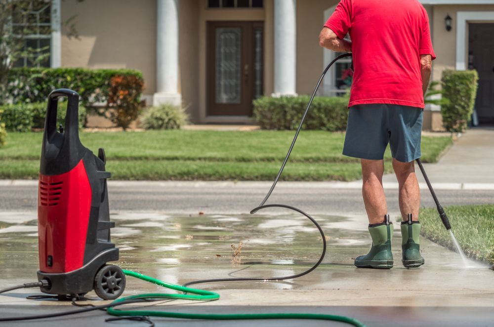 A Man is Using a Pressure Washer to Clean a Driveway in Front of a House — DJ's Pressure Cleaning In Cardwell, QLD
