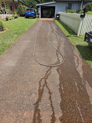 A Hose is Sitting on the Side of a Driveway Next to a House — DJ's Pressure Cleaning In Carruchan, QLD