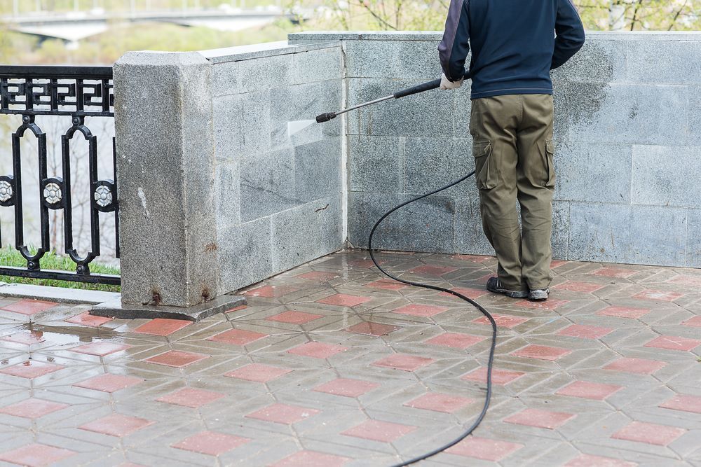 A Man is Using a High Pressure Washer to Clean a Brick Walkway — DJ's Pressure Cleaning In Cardwell, QLD