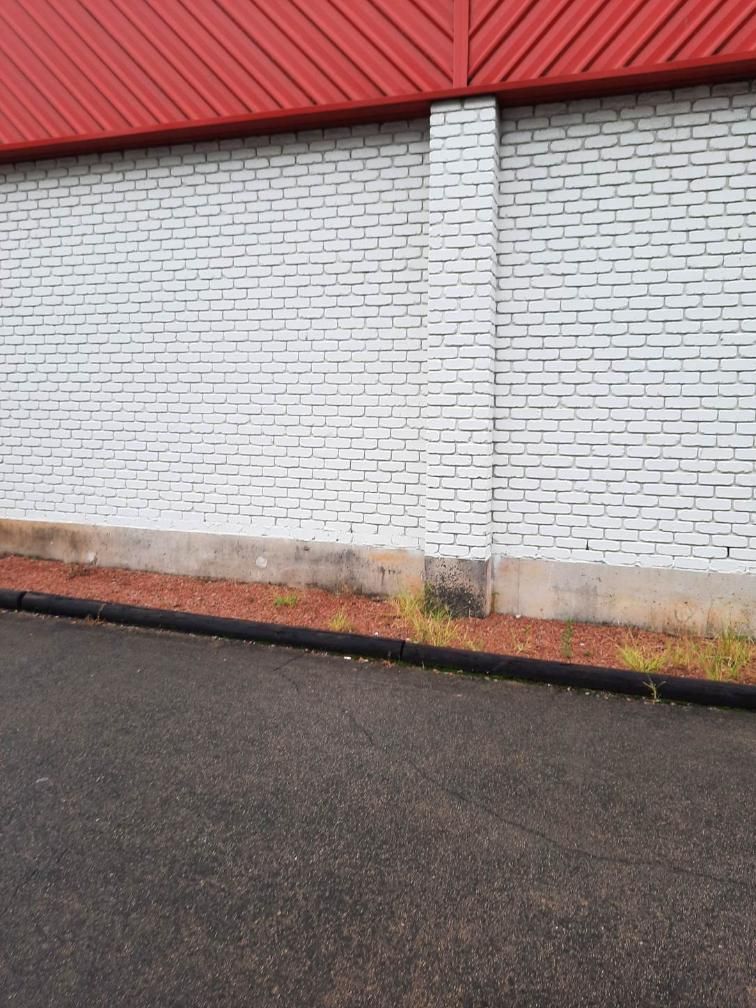 A White Brick Wall With A Red Roof Is Next To A Road — DJ's Pressure Cleaning In Cardwell, QLD