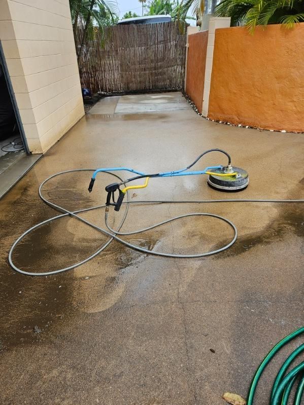A Pressure Washer is Sitting on Top of a Concrete Driveway Next to a Hose — DJ's Pressure Cleaning In Cardwell, QLD