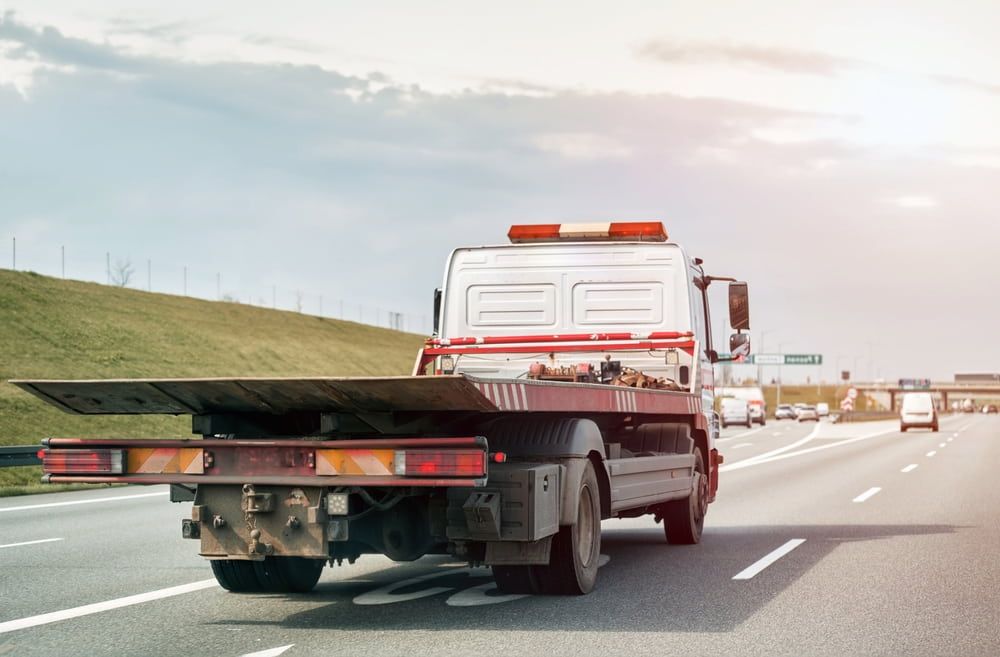 A Tow Truck Is Driving Down A Highway With A Flat Bed  — Newcastle Truck Repairs in Maitland, NSW