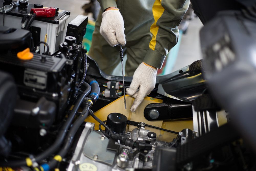 A Man Is Working On A Car Engine With A Screwdriver  — Newcastle Truck Repairs in Thornton, NSW