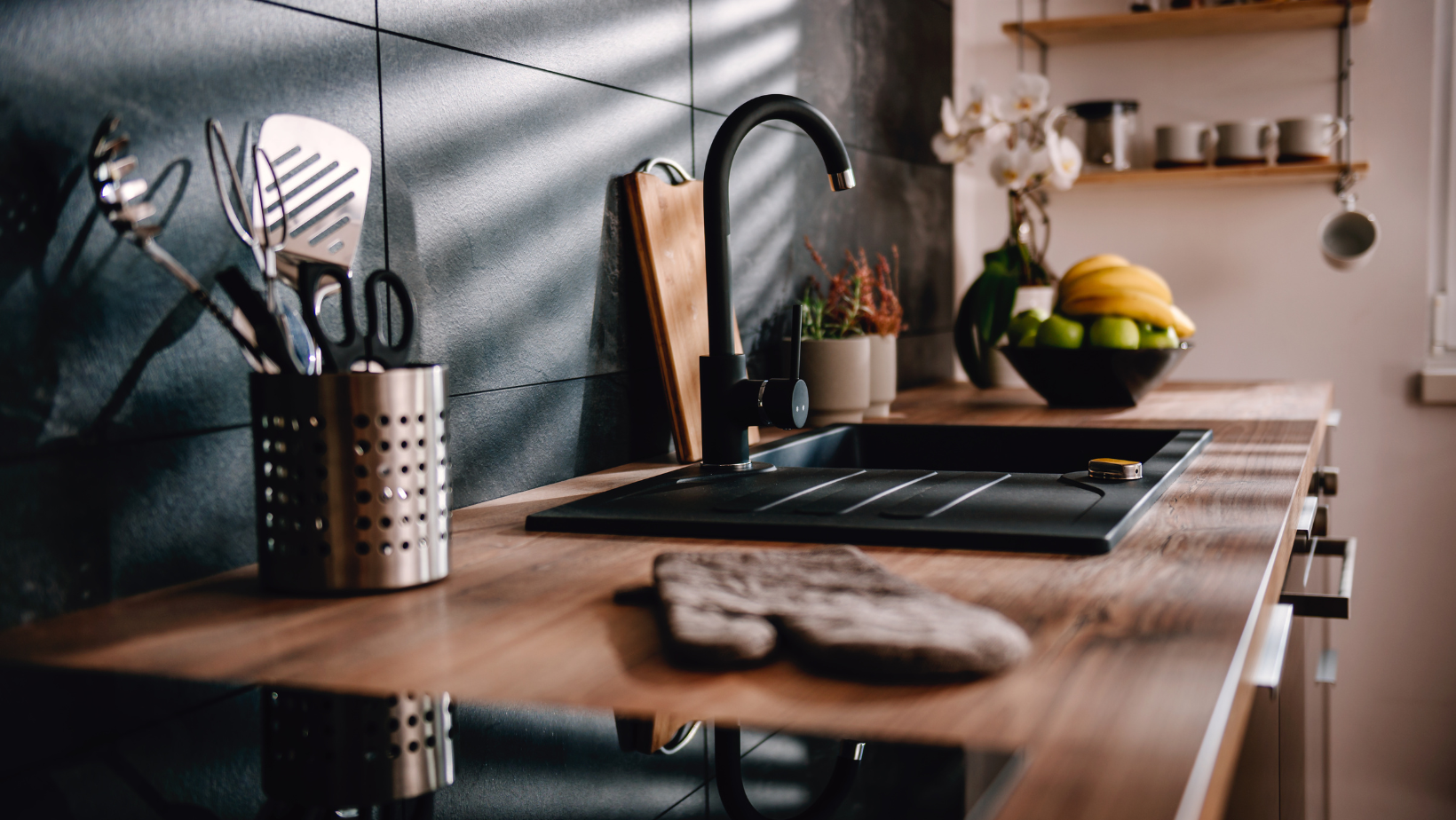 Kitchen counter with sink, utensils, cutting board, and fruit bowl.