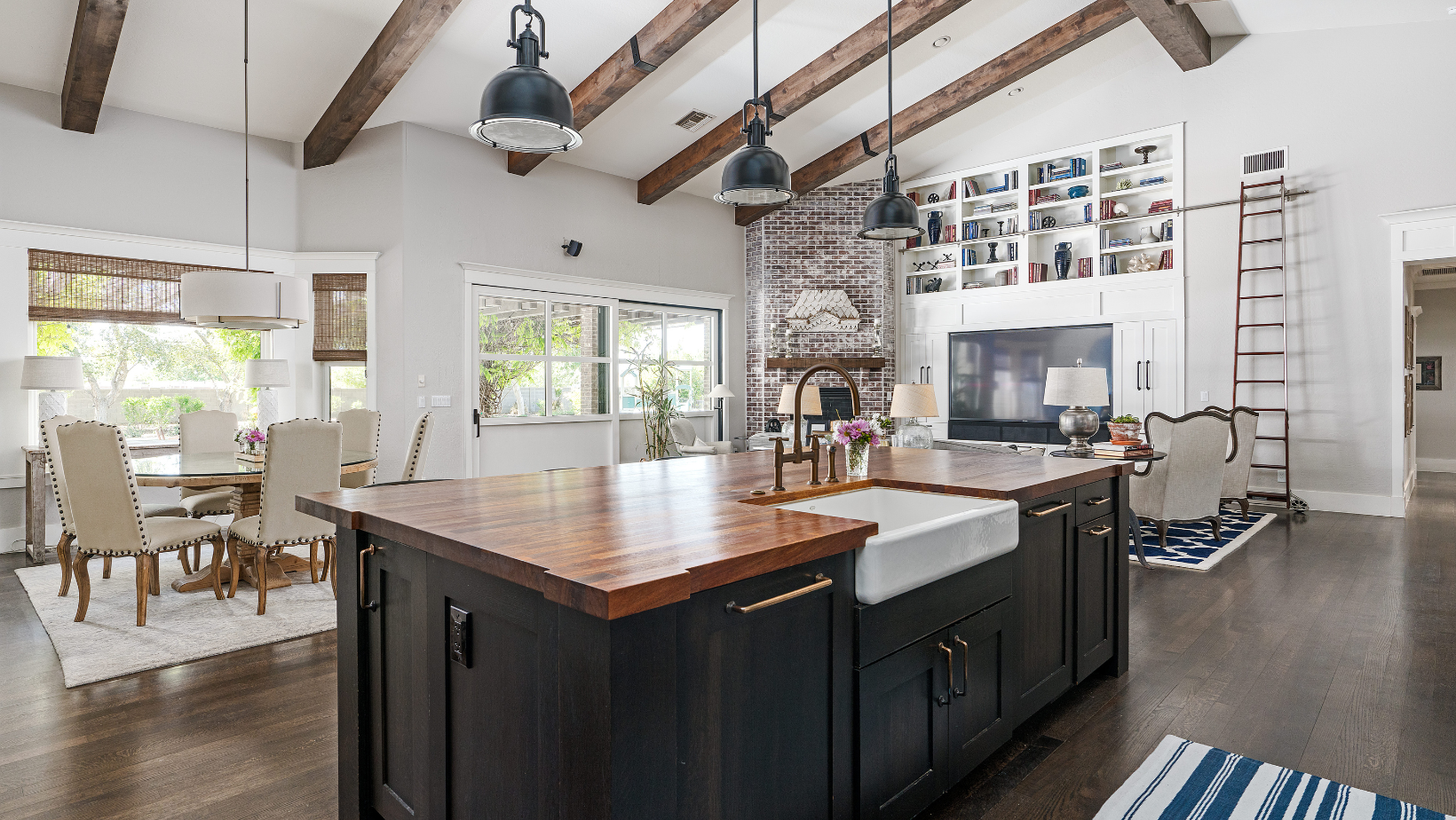 Spacious kitchen with dark island, wooden beams, dining table, and built-in shelving.