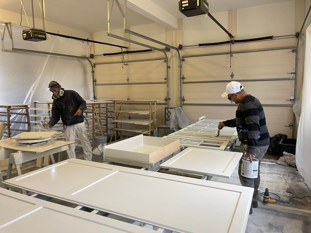 Two men are painting white cabinets in a garage.