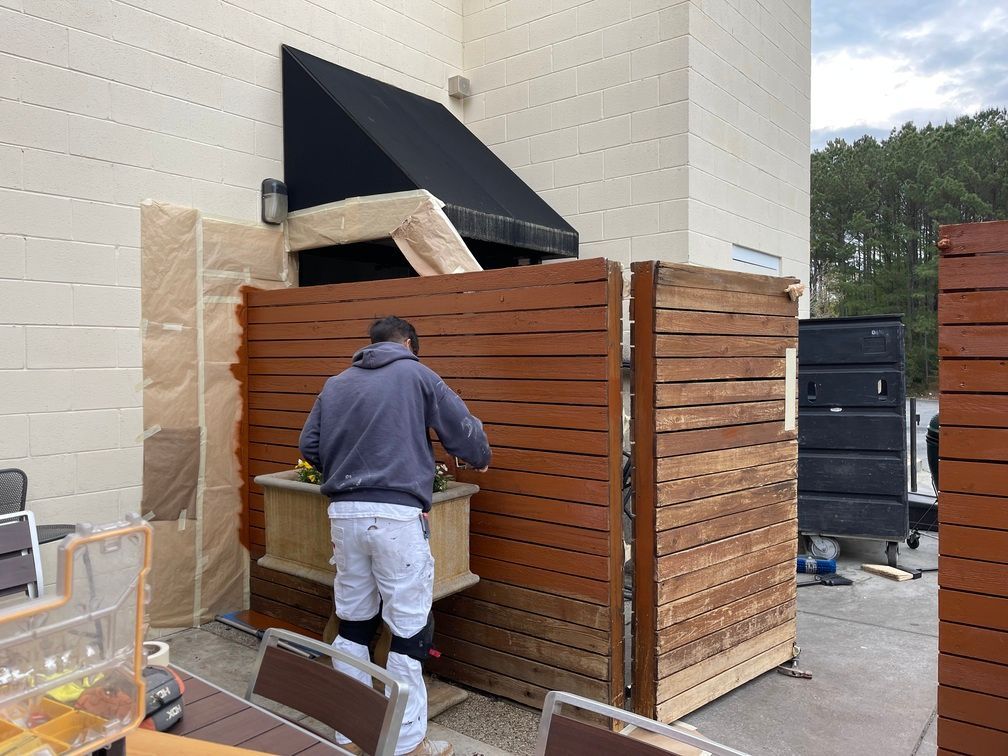 A man is painting a wooden fence outside of a building.