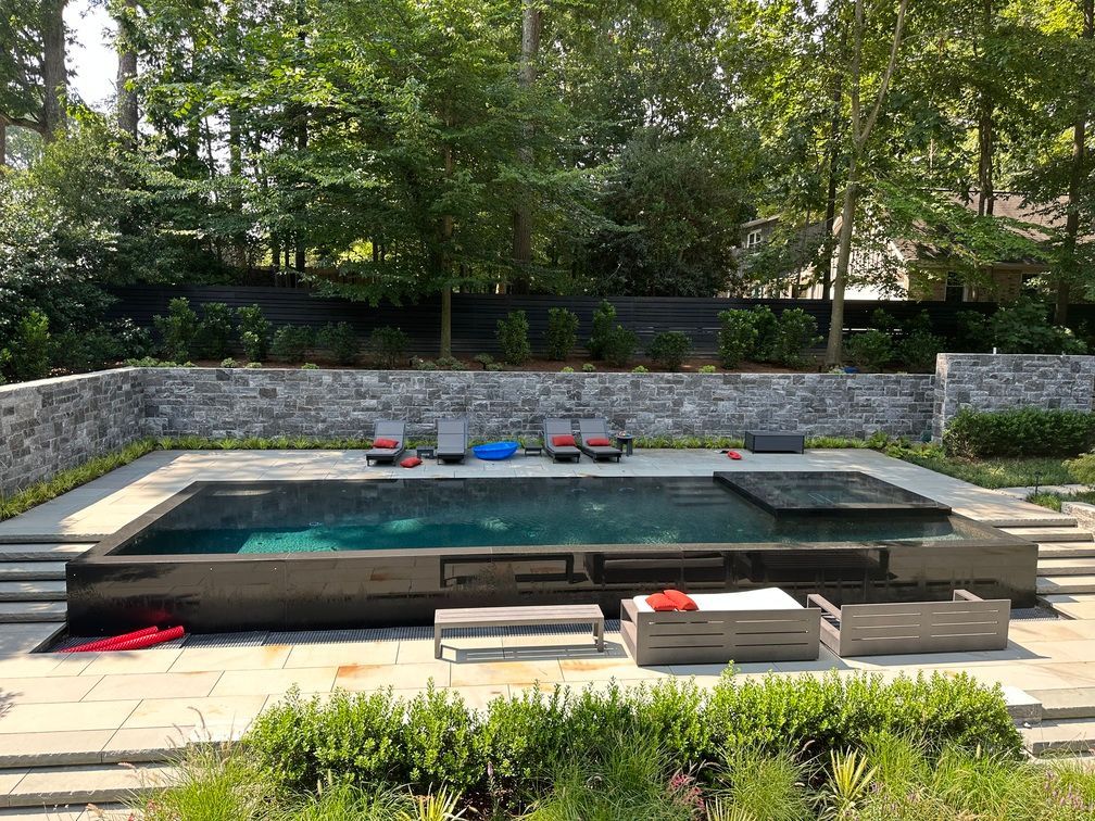 A large swimming pool is surrounded by a stone wall and chairs.
