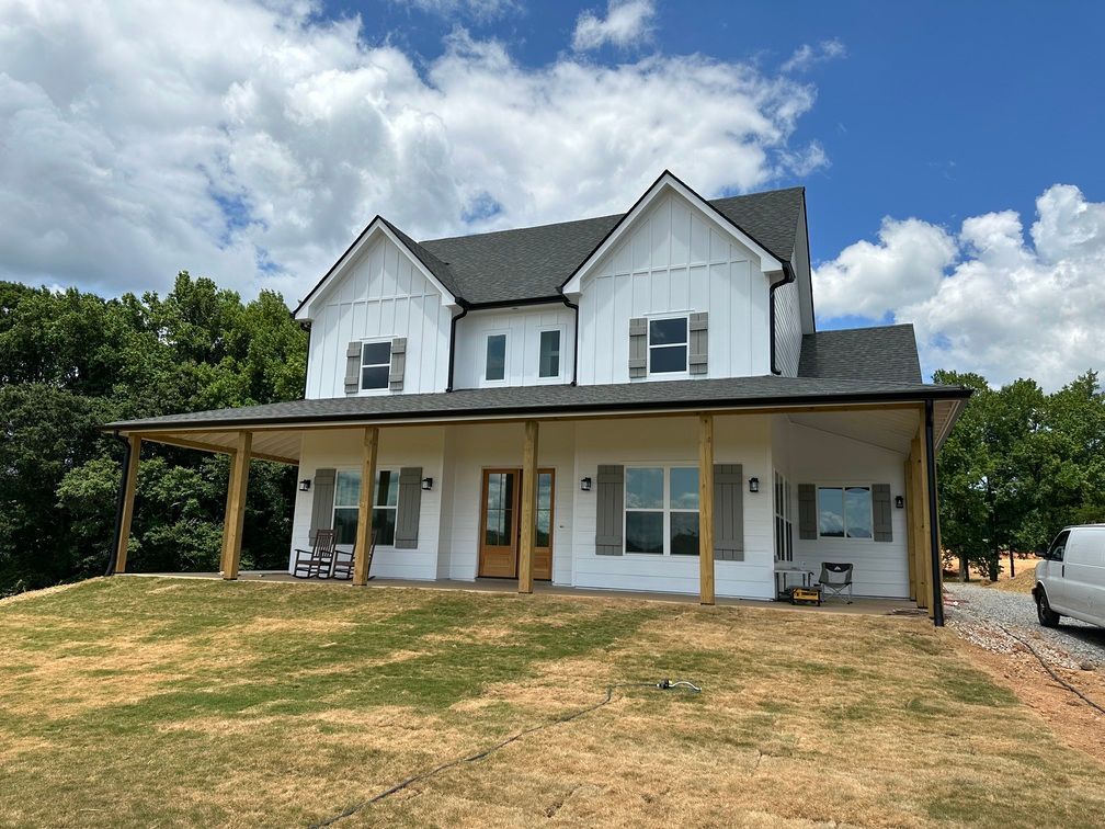 A large white house with a porch and a van parked in front of it.