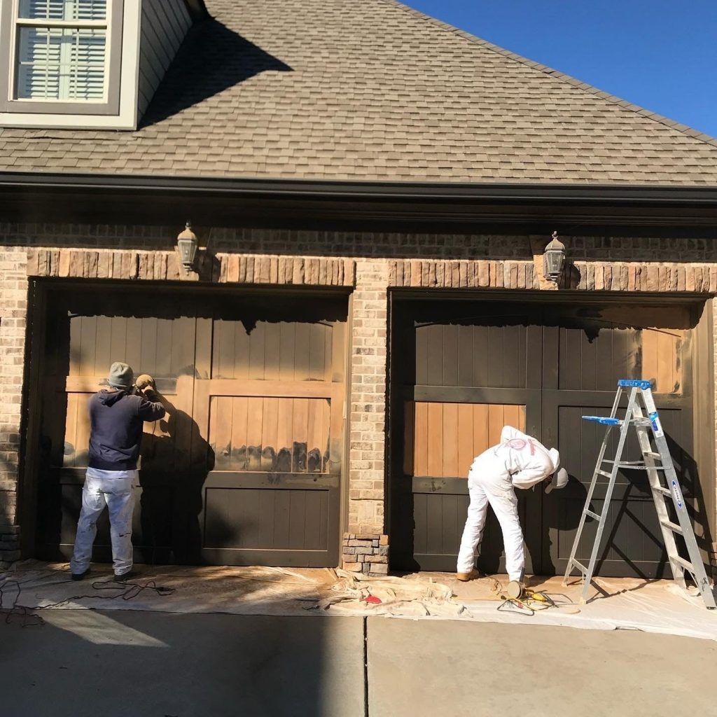Two men are painting the garage doors of a house