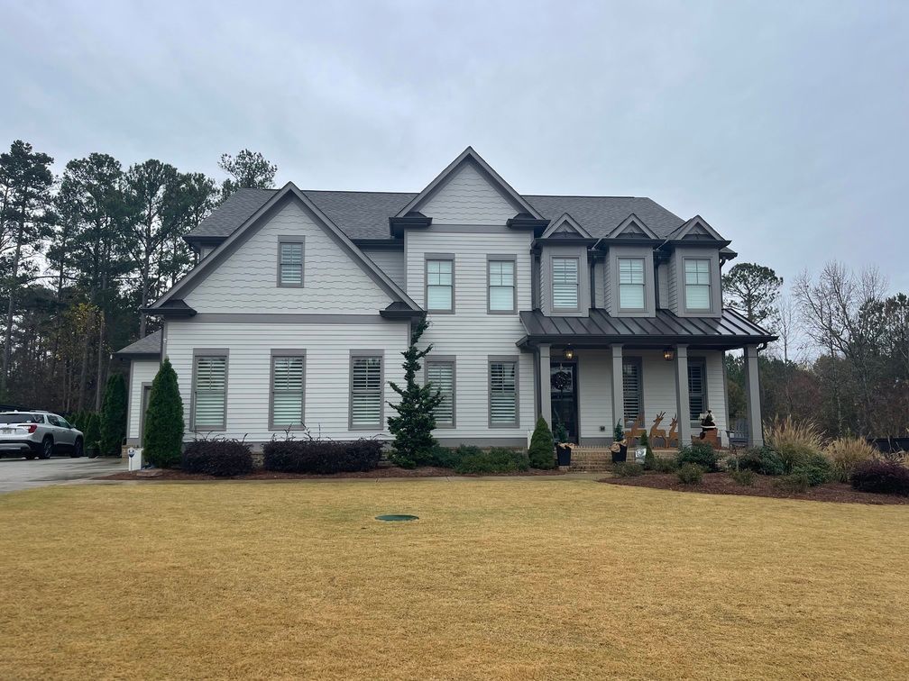 A large white house with a gray roof is sitting on top of a lush green field.