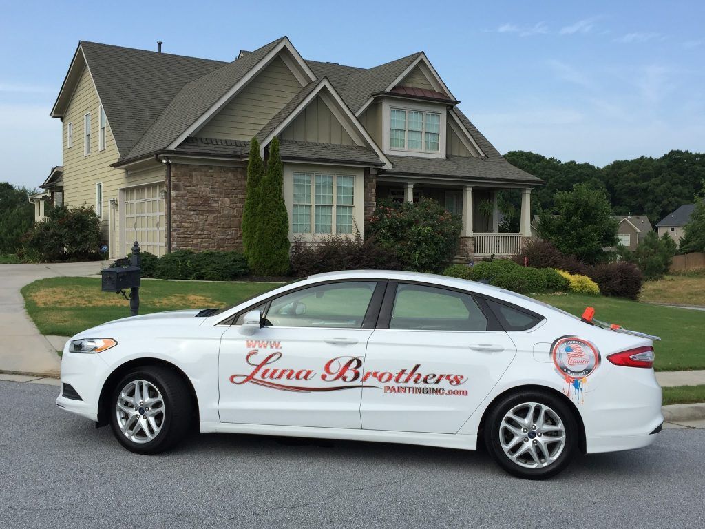 A white luna brothers car is parked in front of a house
