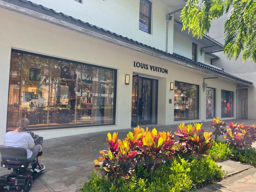 A man is riding a scooter in front of a louis vuitton store.