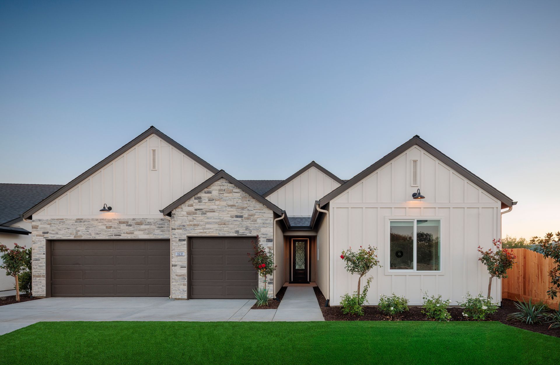Modern single-story new construction home with stone accents, three-car garage, and green lawn.