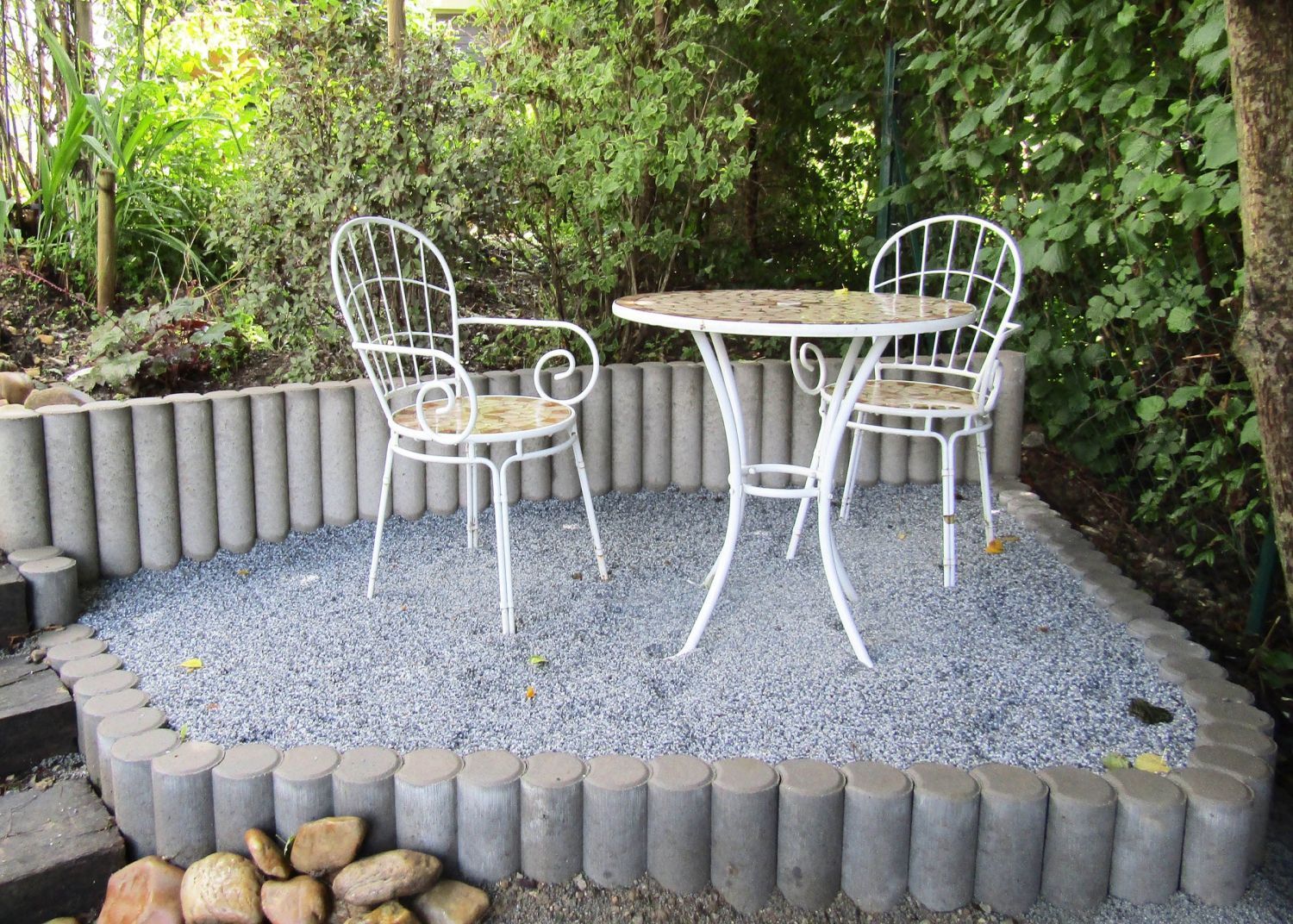 Ein Tisch und Stühle stehen auf Kies in einem Garten.