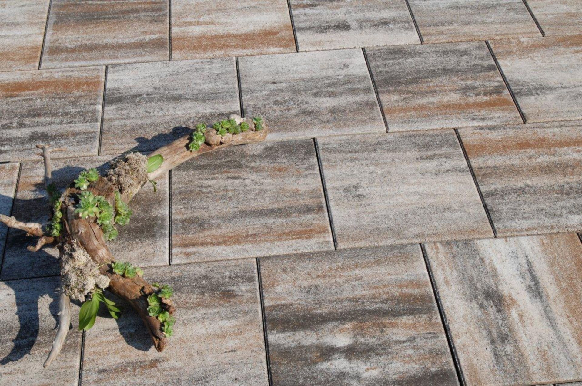 Auf einem Ziegelpflaster liegt ein Stück Holz.