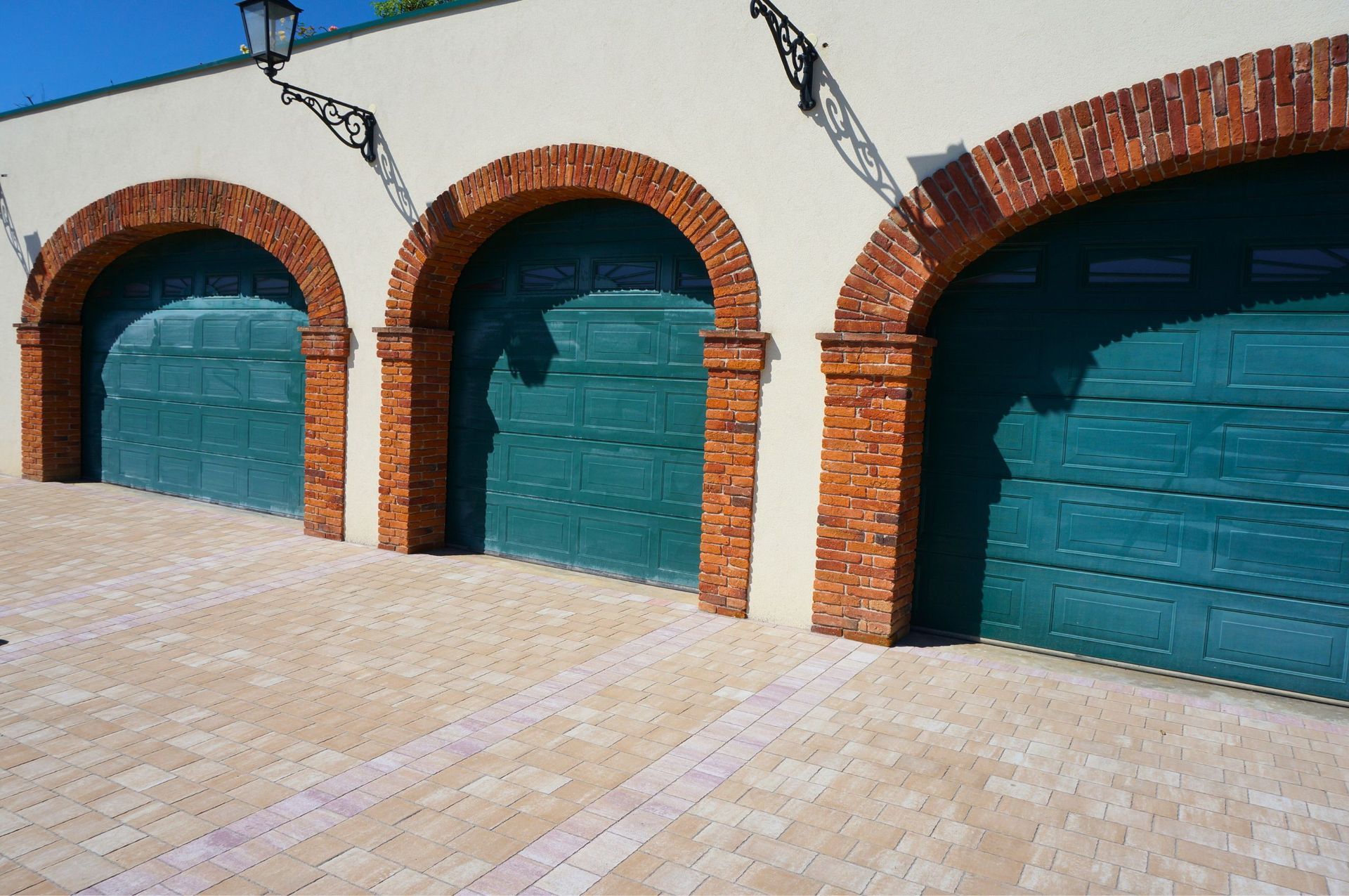 Drei grüne Garagentore mit Bögen auf einem Backsteingebäude