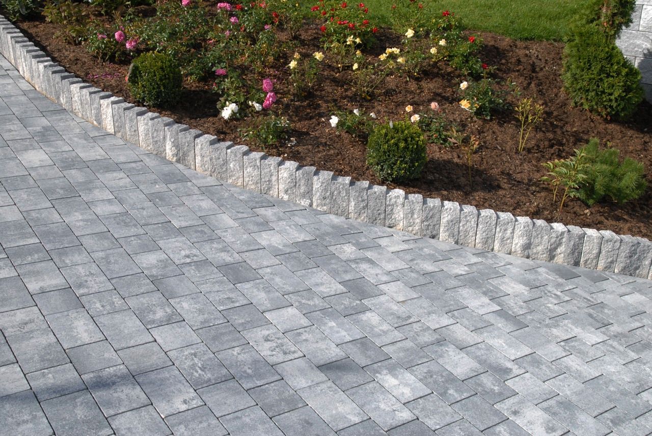 Eine Auffahrt mit Ziegelsteinrand und Blumen im Hintergrund.