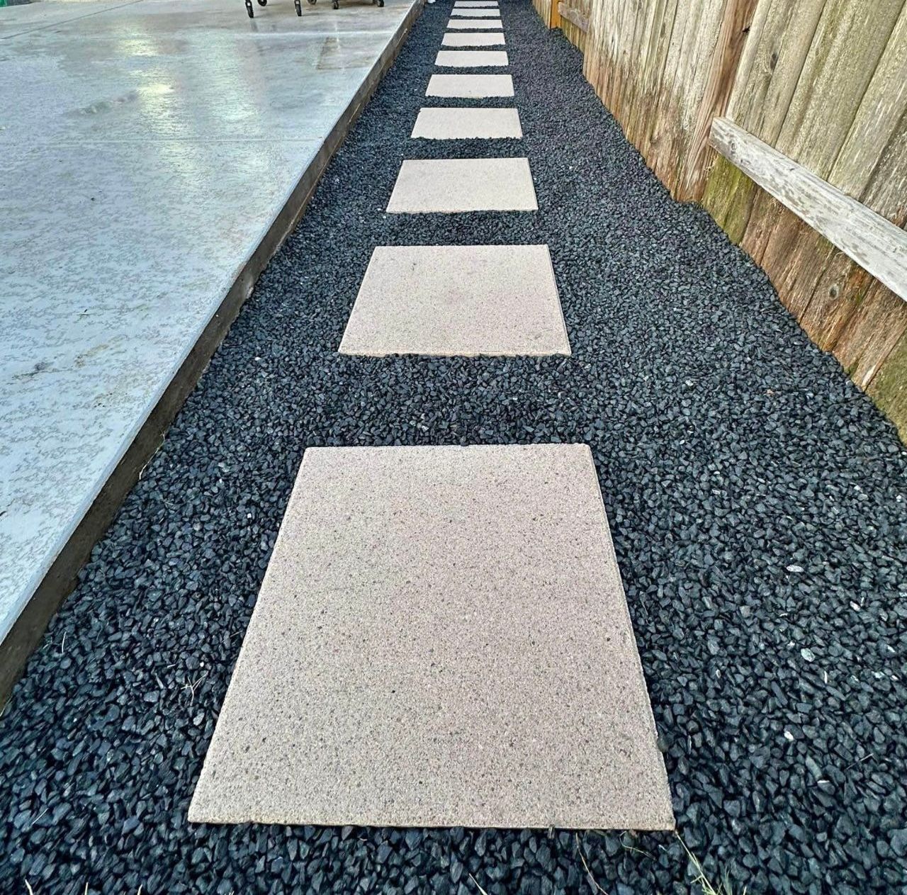 A row of stepping stones on a gravel path next to a fence.