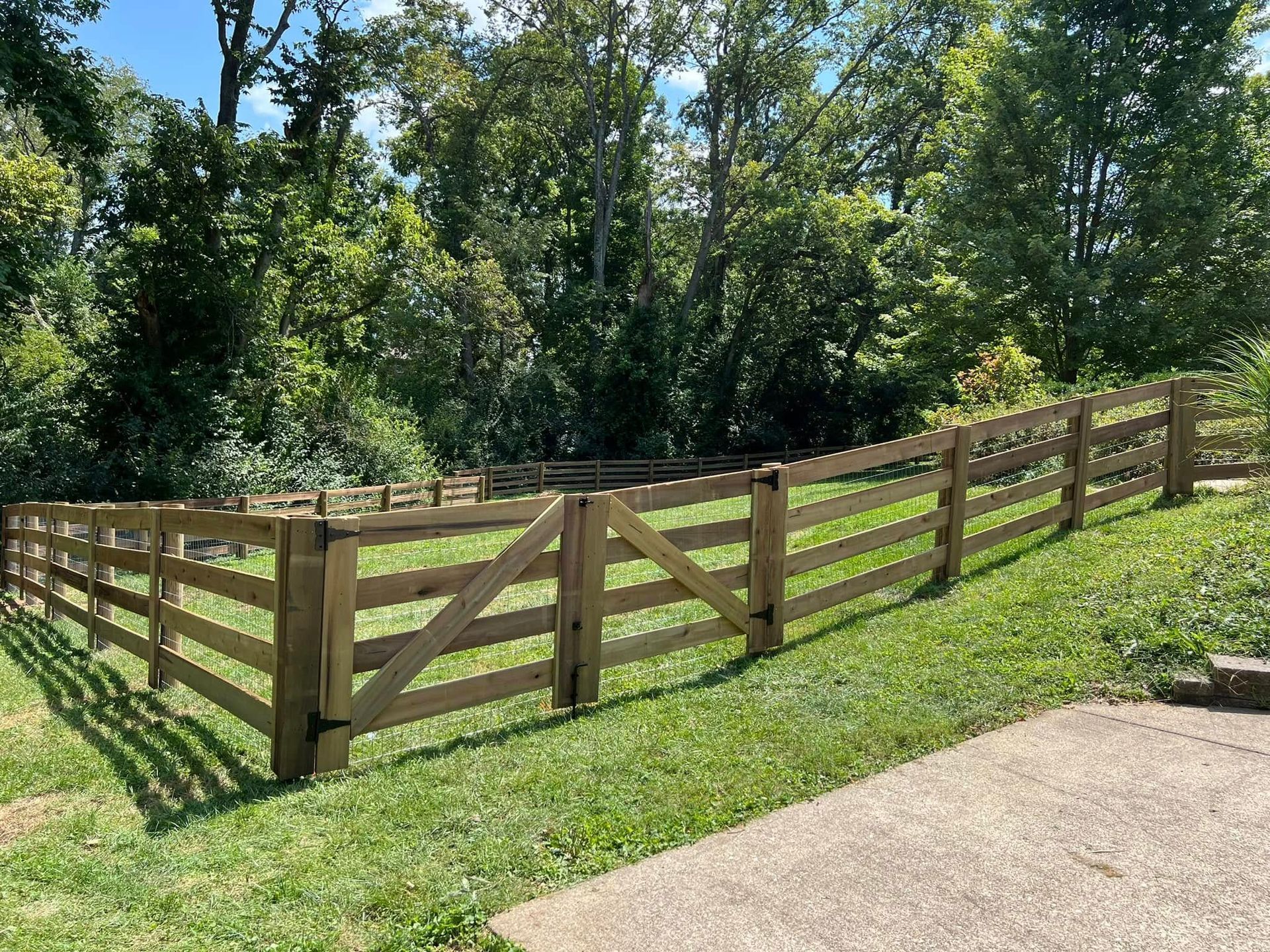 A small shed is sitting in the middle of a lush green yard next to a wooden fence.