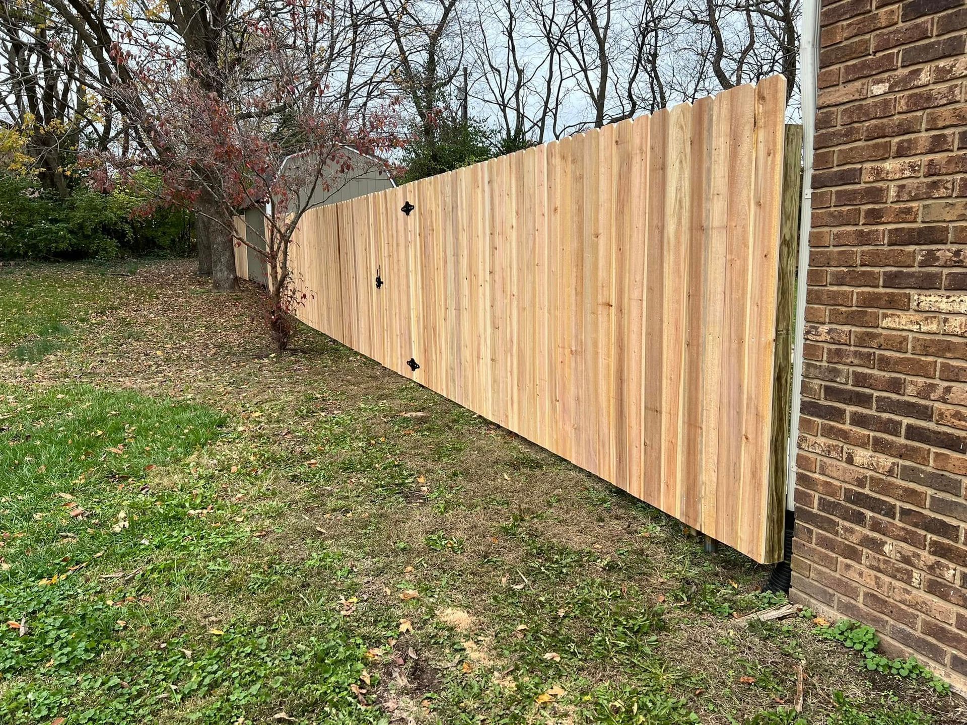 A wooden fence is sitting next to a brick wall in a yard.