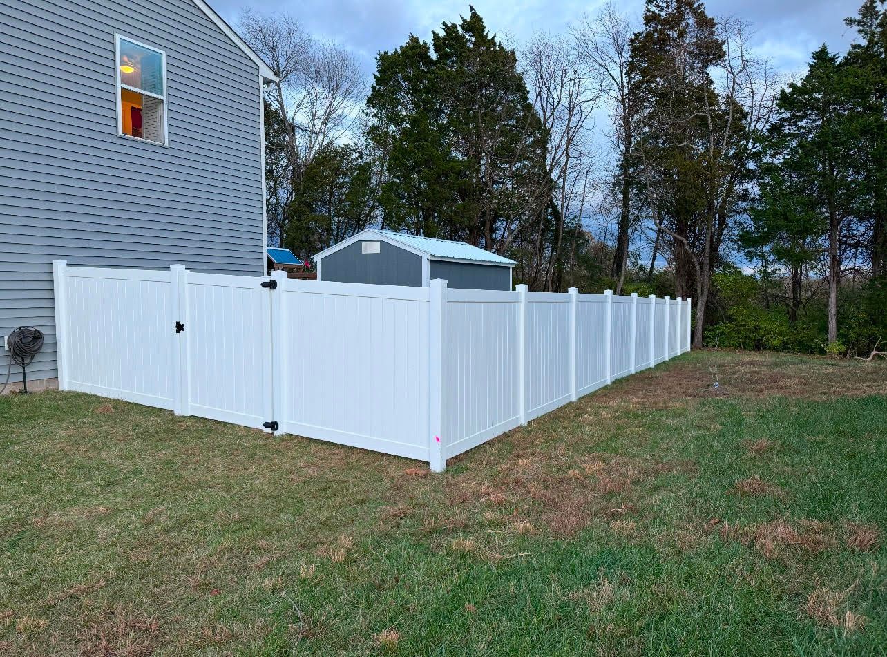 A wooden fence is surrounding a concrete area with a water tower in the background.