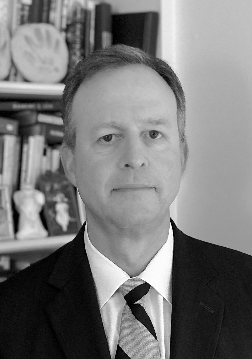 A man in a suit and tie is standing in front of a bookshelf.