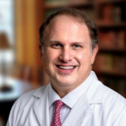 A man in a lab coat and tie is smiling for the camera.