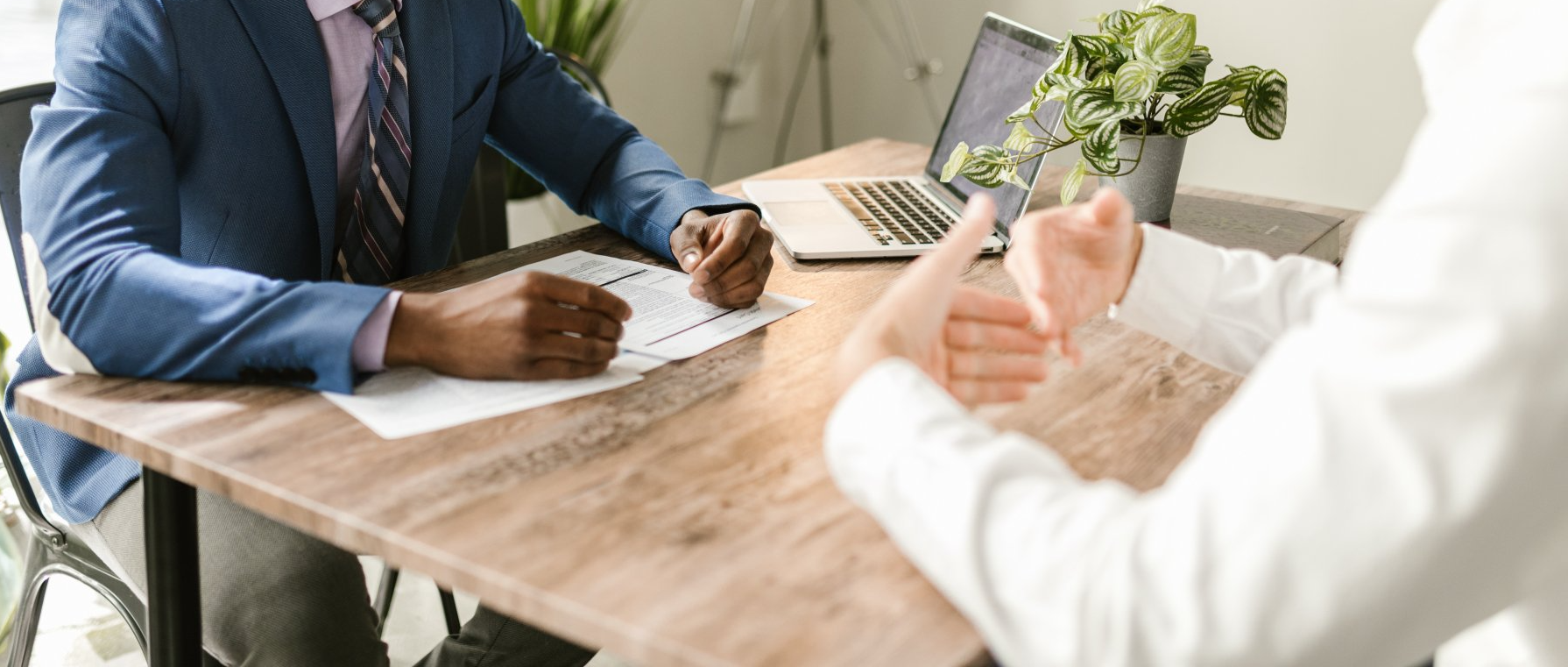 A man in a suit and tie is sitting at a table talking to a woman.