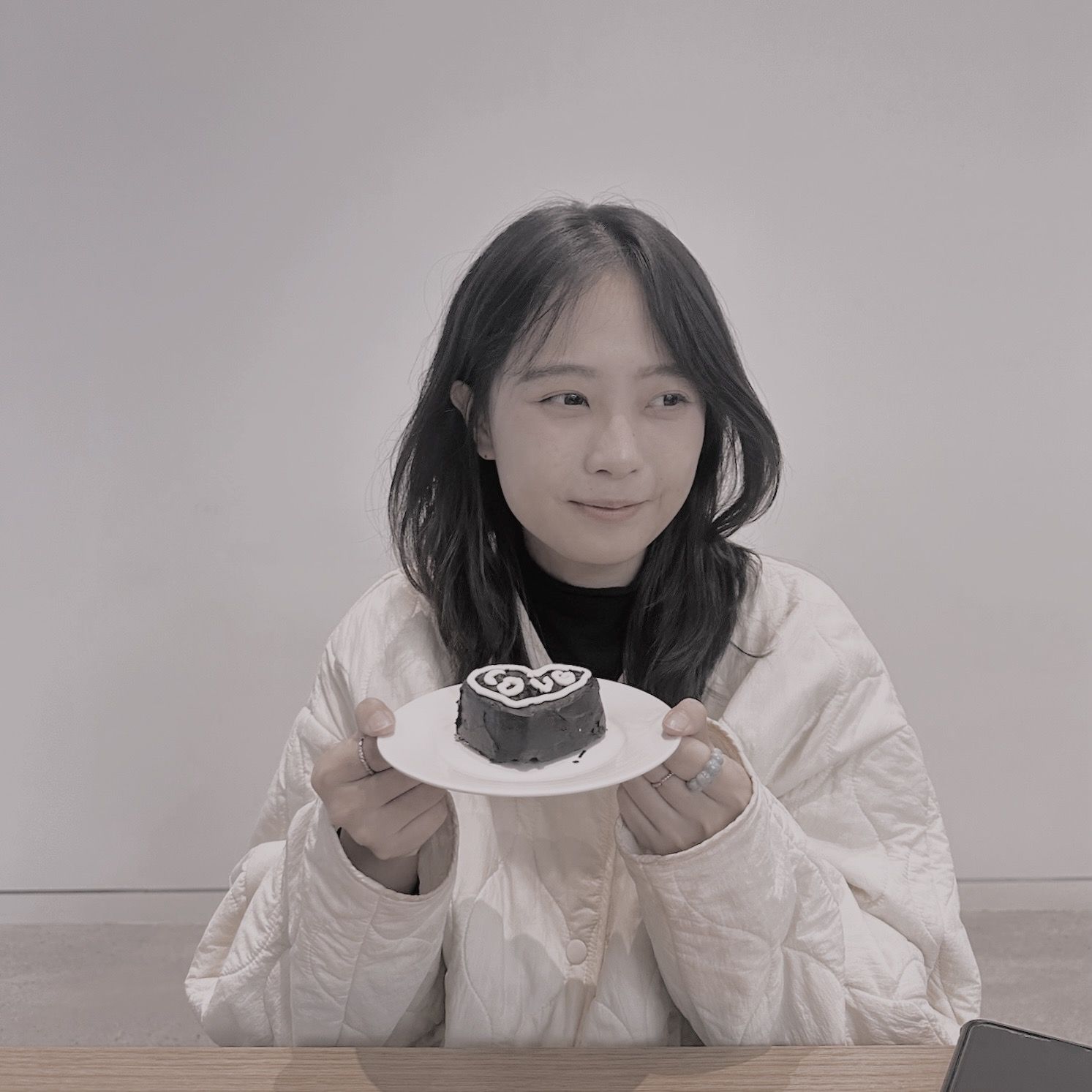 黑白照片中，一名身穿白色夾克的女子微笑著。